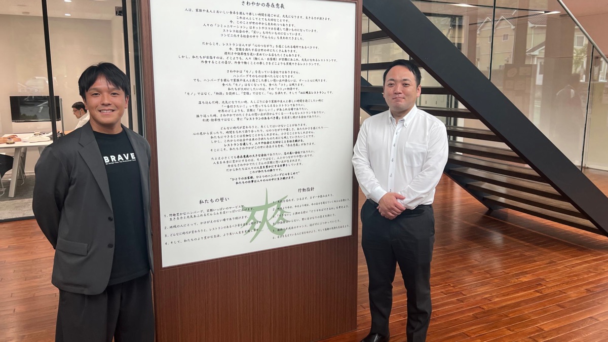 さわやかの存在意義が書かれたパネルの前に並ぶ、さわやか株式会社の小沢様とブレイブテクノロジーの石井