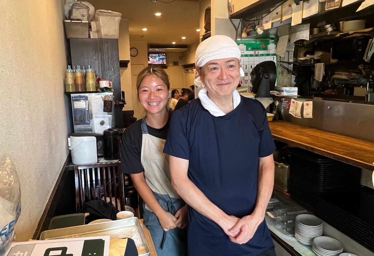 厨房の前で笑顔を見せる髙橋店長とスタッフ